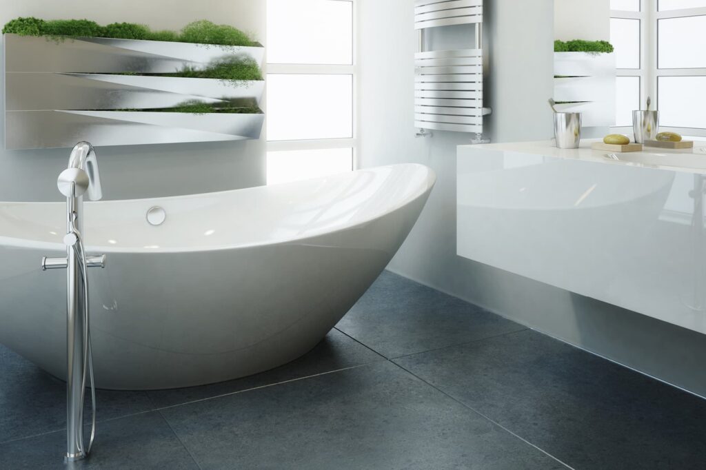 Ein modernes Badezimmer mit einer freistehenden weißen Badewanne, dunklem Fliesenboden und einem Waschtisch mit einem Spiegel, der grüne Pflanzen reflektiert, symbolisiert die hochwertige Sanitärtechnik von Steirertech.
